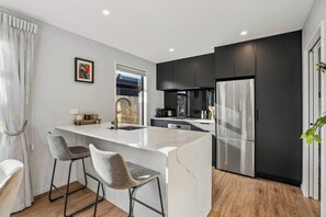 A modern kitchen with a central island, bar stools, a refrigerator, and a window. - Base Northlake | Peaceful with Mountain Views (Wānaka)