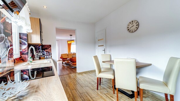 A modern kitchen with a built-in oven, a dining area with a round table and chairs, and a wall clock. - Apartament nr 32 by Interhome (Gliwice)