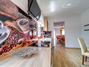 A modern kitchen with a large flat-screen TV, wooden flooring, and a dining area with a chair. - Apartament nr 32 by Interhome (Gliwice)