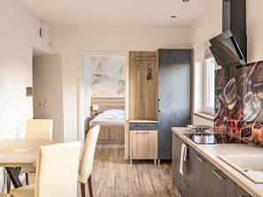 Une chambre d’hôtel moderne et compacte, dotée d’une kitchenette, d’un coin repas et d’un lit placé devant un mur orné d’un motif géométrique.