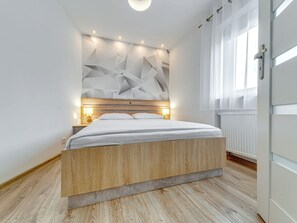 A modern bedroom with a wooden bed, geometric wall design, and a window with curtains. - Apartament nr 32 by Interhome (Gliwice)