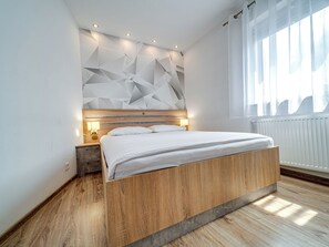 A modern bedroom with a wooden bed, geometric wall design, and a window with curtains. - Apartament nr 32 by Interhome (Gliwice)