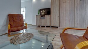Ein modernes Wohnzimmer mit Ledersofas, einem Glastisch und einem Flachbildfernseher auf einer Holzkommode.