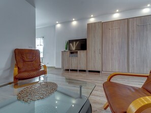 Ein modernes Wohnzimmer mit Ledersofas, einem Glastisch und einem Flachbildfernseher auf einer Holzkommode.
