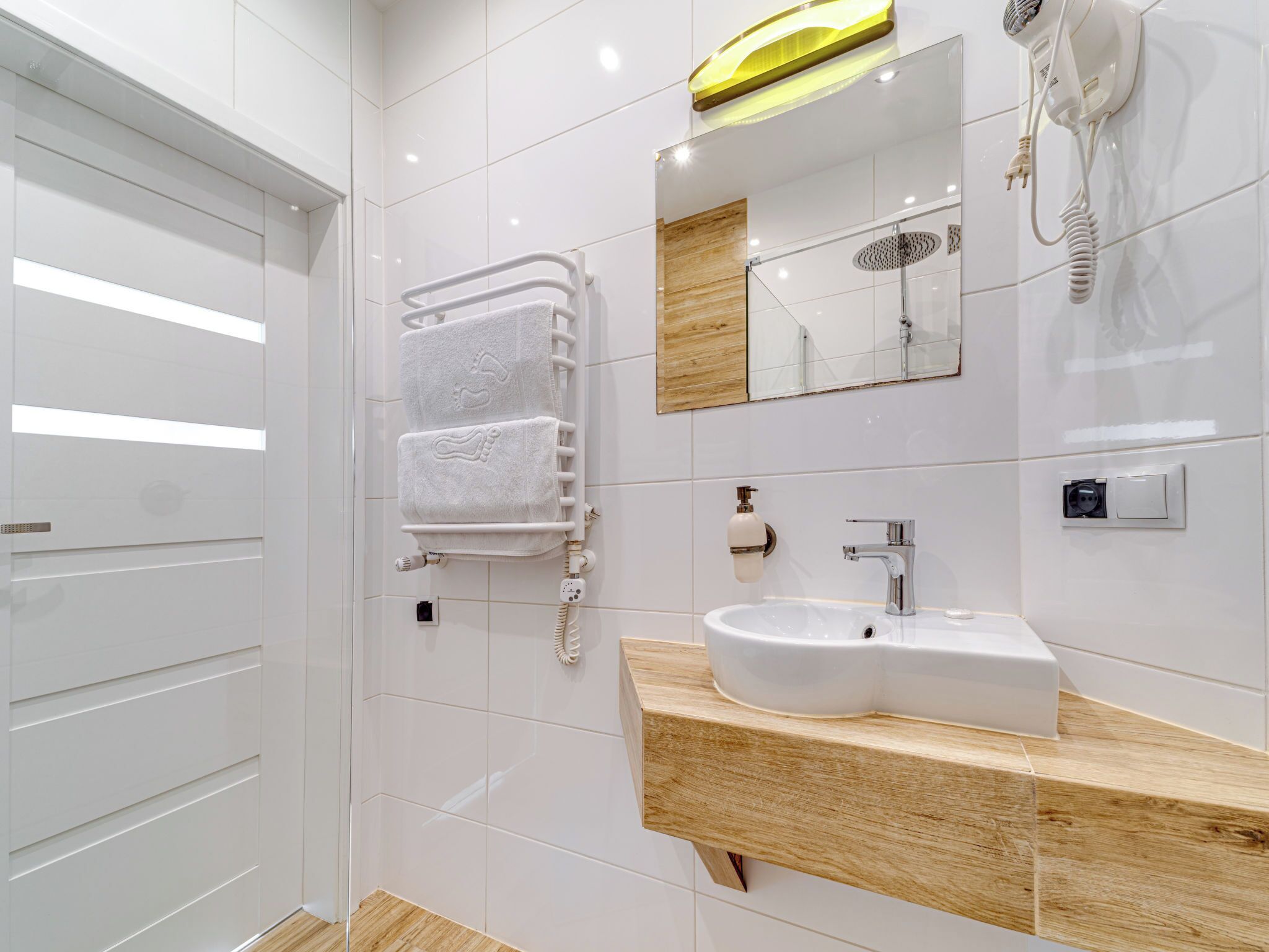 Une salle de bain moderne avec un lavabo blanc, un miroir, un porte-serviettes et un sèche-cheveux.