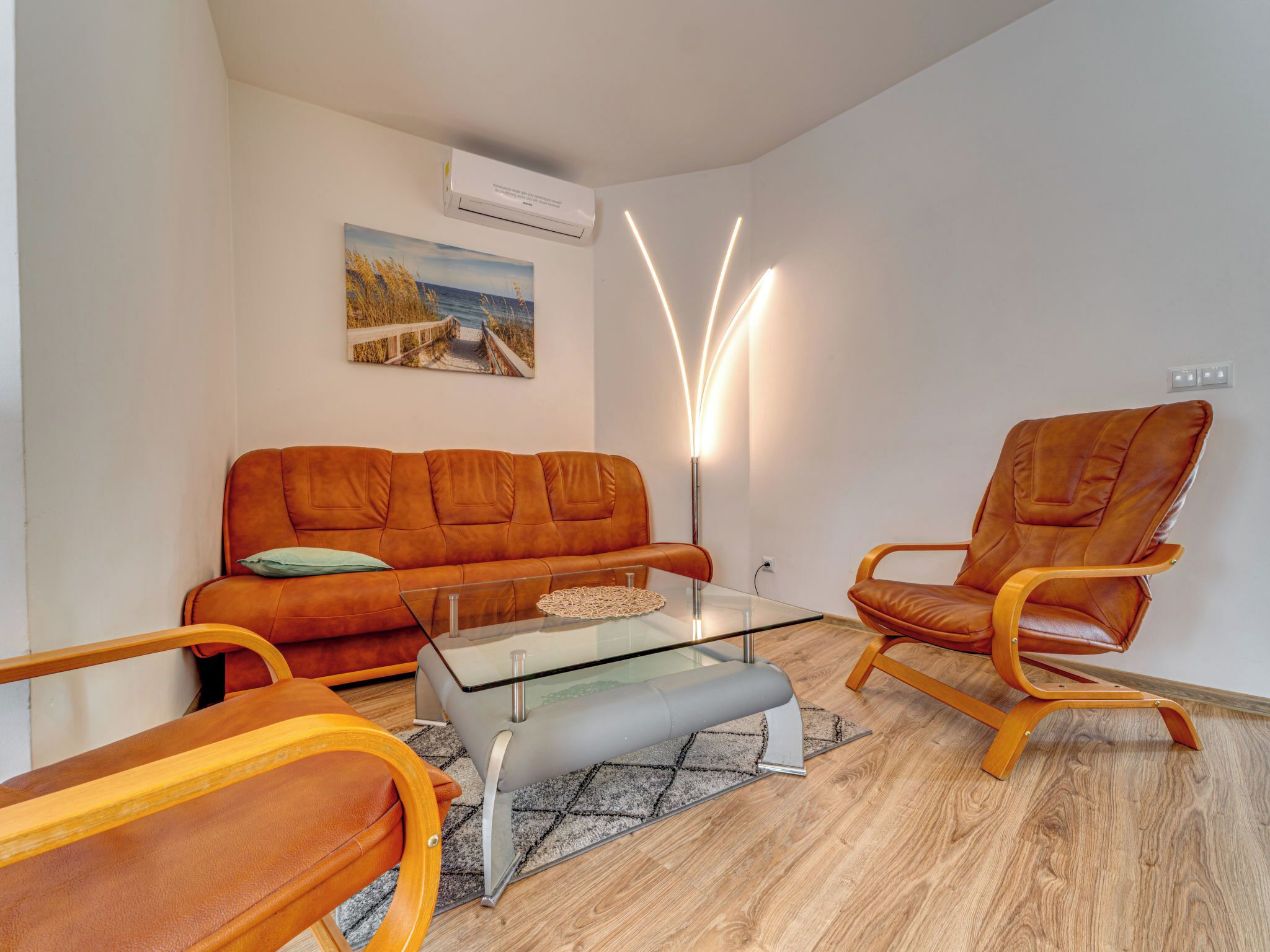 Un salon moderne avec un canapé, des fauteuils, une table basse en verre et un tableau accroché au mur.