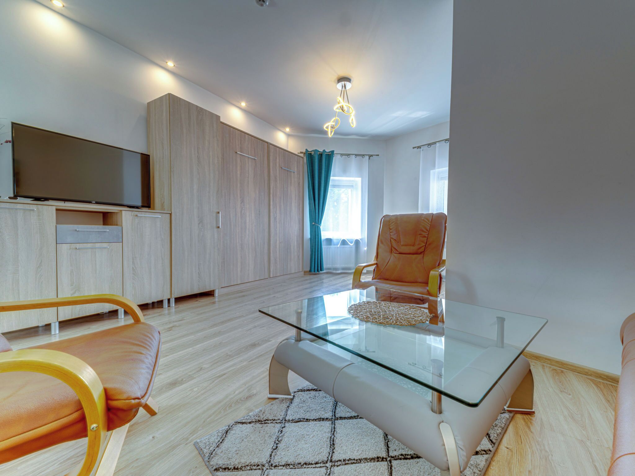 Una sala de estar moderna con una mesa de centro de vidrio, sofá de cuero, armarios de madera y un televisor de pantalla plana.