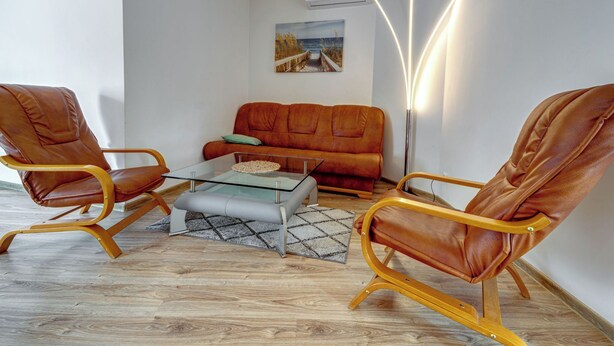 Ein modernes Wohnzimmer mit Ledersesseln, einem Glastisch, einer Couch und einem Gemälde an der Wand.