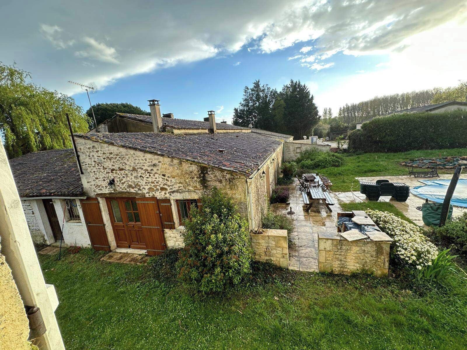 Une maison en pierre avec un toit en tuiles, une porte en bois et un petit jardin agrémenté d’une piscine et de mobilier d’extérieur.