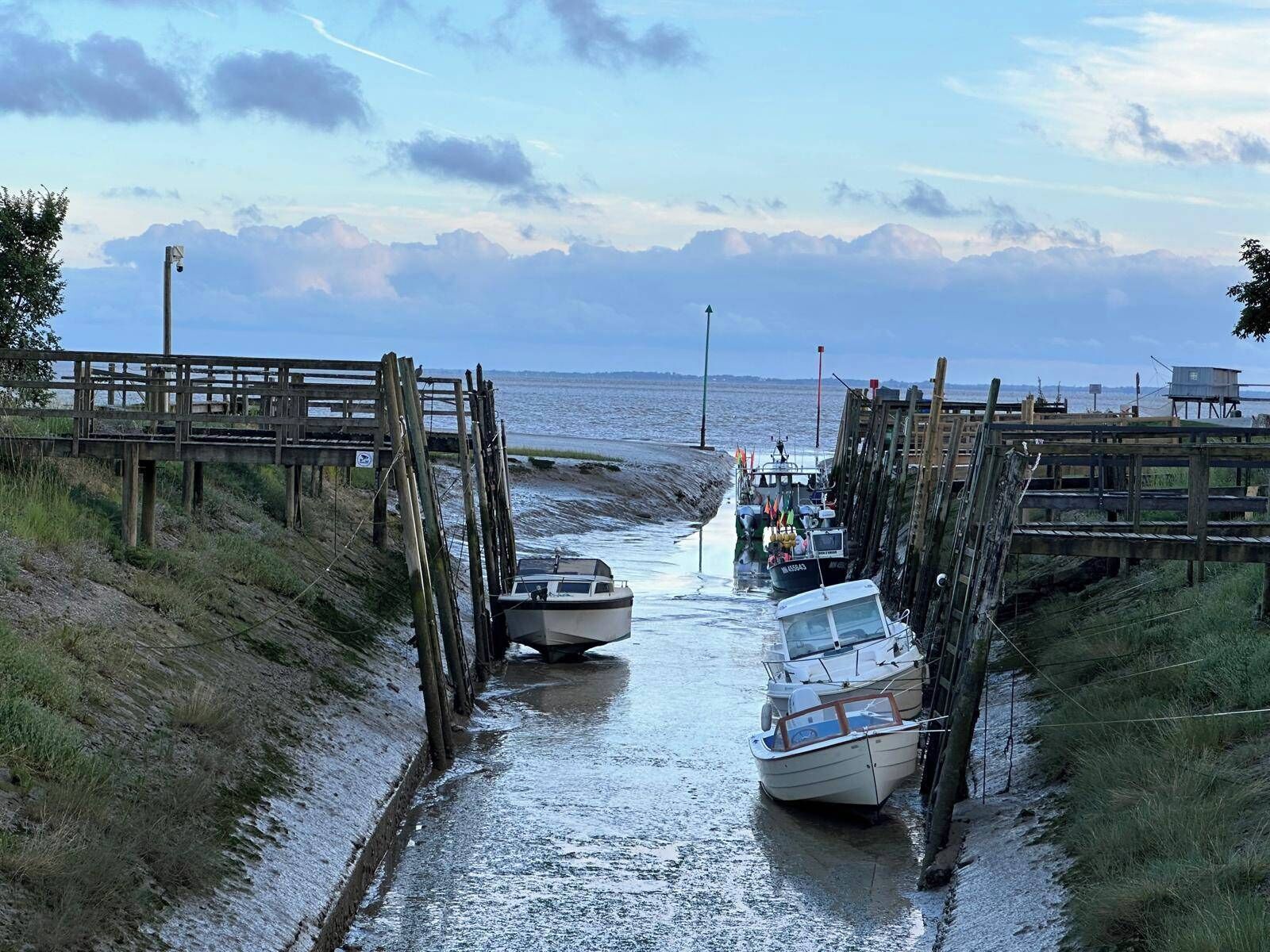 A coastal pier with boats docked, a wooden walkway, and a view of the sea.