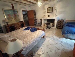 A bedroom with a bed, a dresser, a chair, a desk, a fireplace, and a painting on the wall.