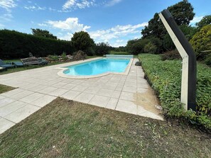 A swimming pool with a tiled deck, surrounded by greenery and trees.