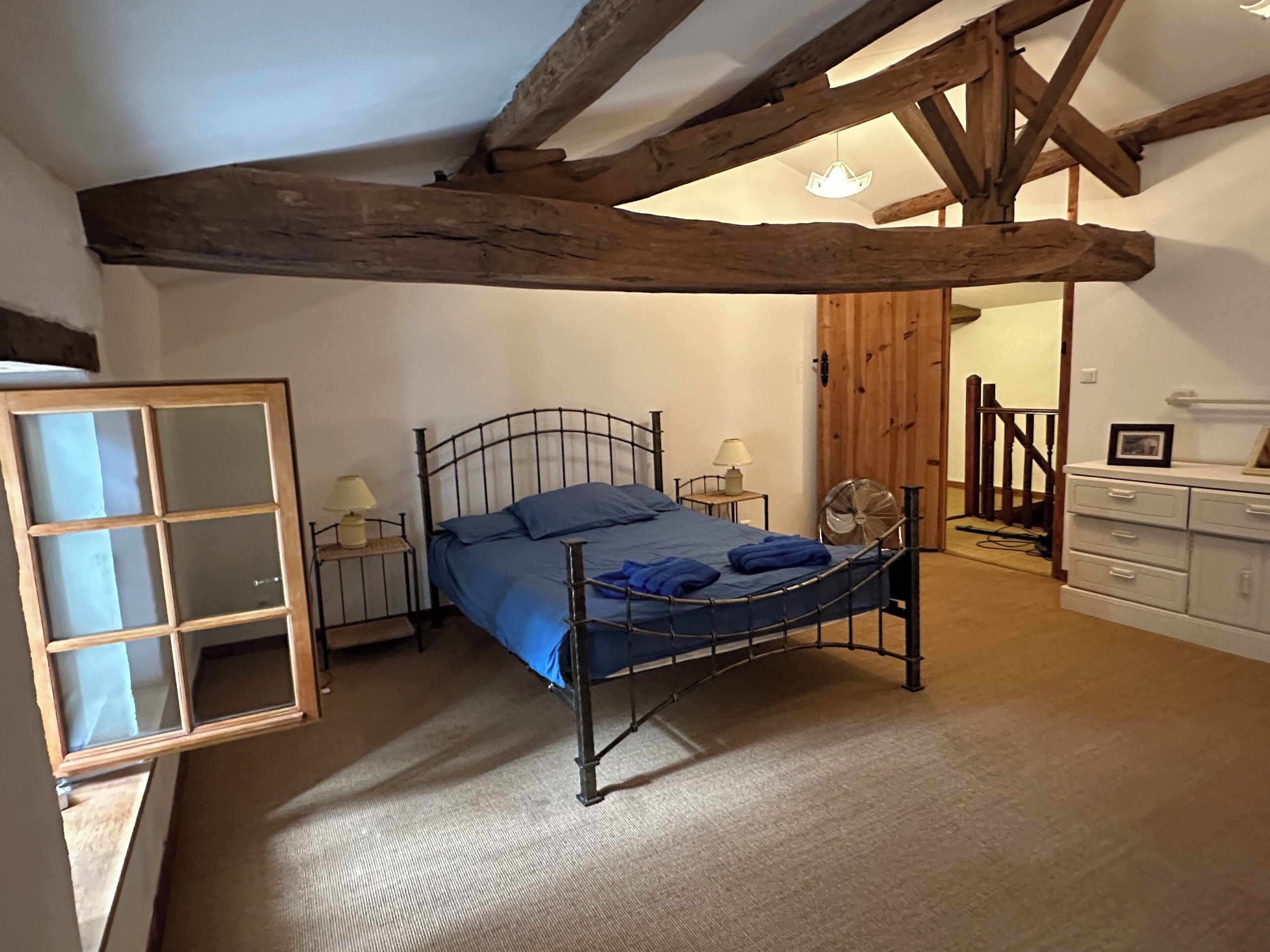 A bedroom with a metal bed frame, a wooden ceiling, a white dresser, and a door leading to another room.