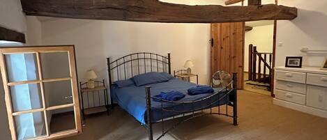 Une chambre avec un lit en métal, un plafond en bois, une commode blanche et une porte donnant sur une autre pièce.