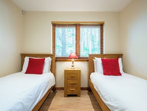 A twin room with two beds, a nightstand with a lamp, and a window with blinds. - Pine Marten Lodge by Interhome (Ballater)