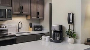 Ett modernt kök med mörka skåp, en mikrovågsugn, en brödrost, en kaffebryggare och en telefon som sitter på väggen.