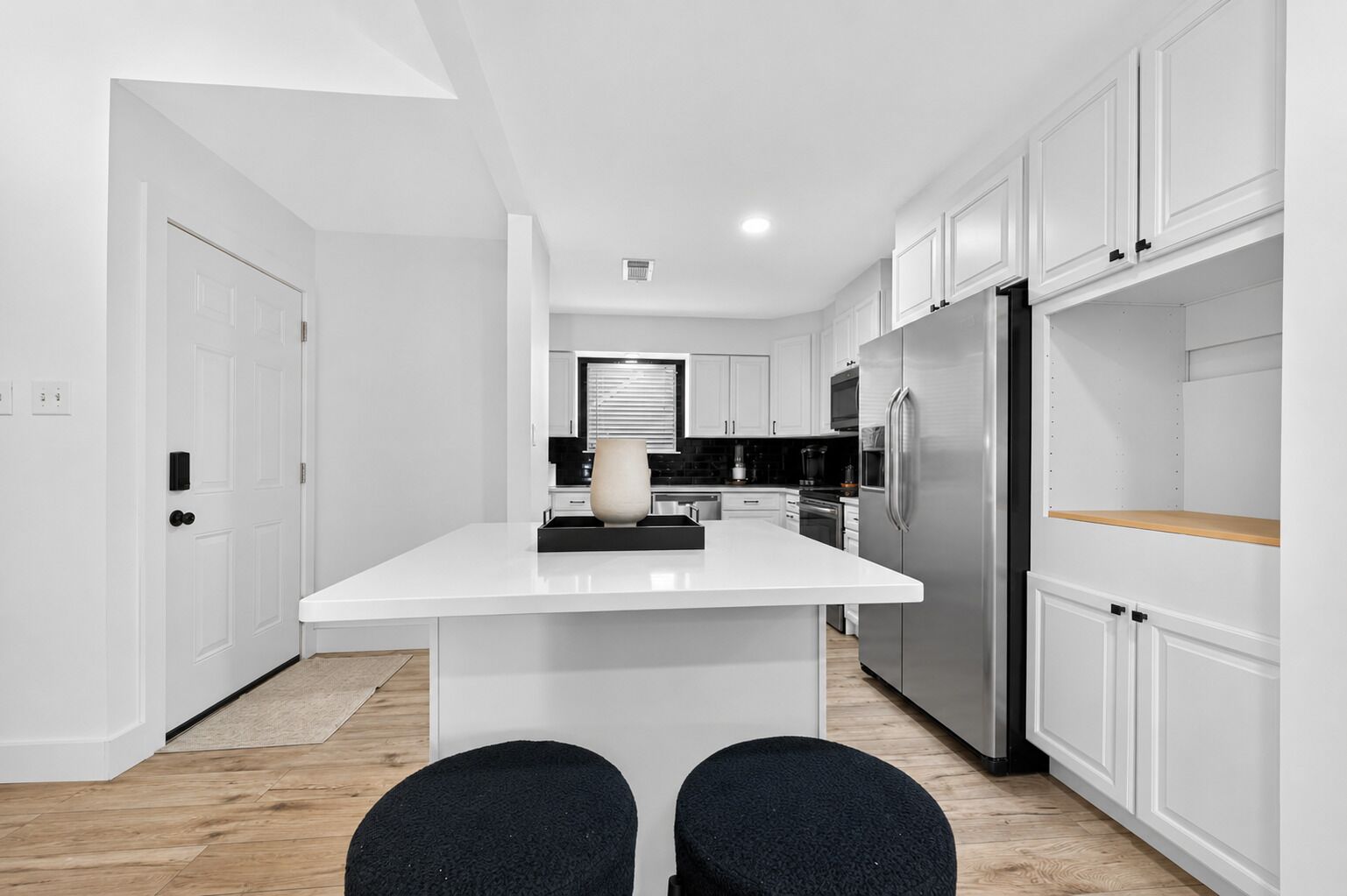 A modern kitchen with white cabinetry, a central island, and a stainless steel refrigerator.