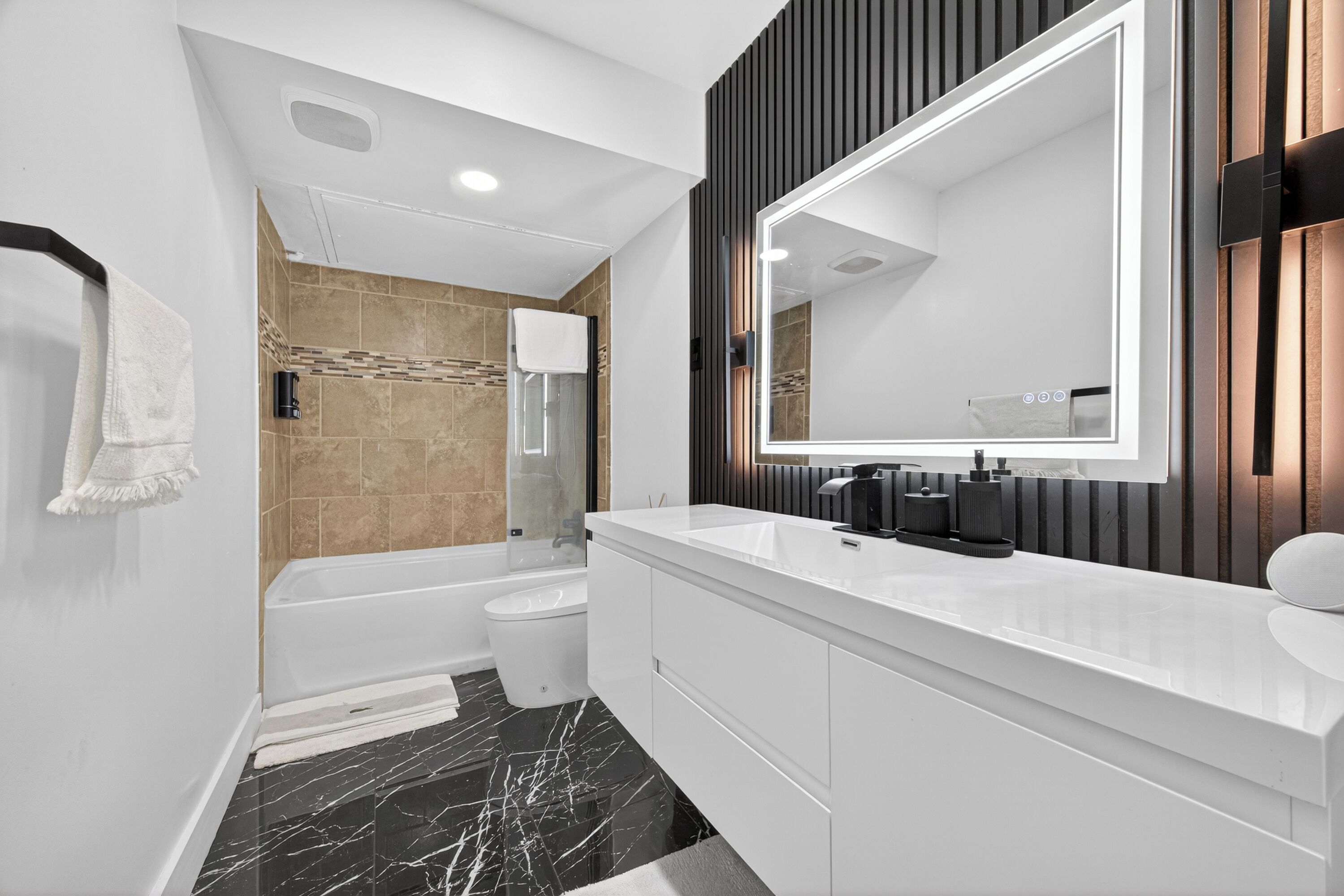 A modern bathroom with a large mirror, a bathtub, a toilet, and a shower area.