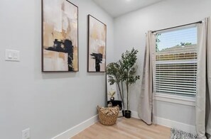 Ein Zimmer mit großem Fenster, einem Blumentopf und zwei abstrakten Bildern an der Wand.