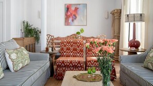 Un salon avec des canapés à rayures, un canapé à motifs, une table basse ornée d’un vase de fleurs et un tableau accroché au mur.