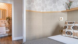 Une chambre à coucher comprenant un lit, une table de chevet, un miroir et une étagère murale ornée d’un vase de fleurs.