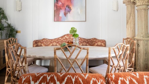 Un coin repas avec une table ronde, des chaises en osier, un canapé à motifs et une colonne décorative.