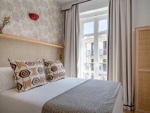 A hotel room with a bed, a window with curtains, a wall-mounted red decorative object, and a view of a building outside. - Hommyhome O´Donnell in the heart of Seville (Sevilla)