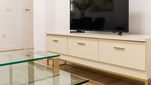 Un salon moderne avec un téléviseur à écran plat posé sur un meuble blanc, une table basse en verre et une porte dotée d’une poignée.