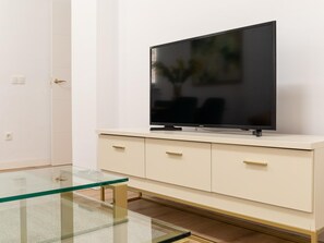 Ein modernes Wohnzimmer mit Flachbildfernseher auf einem weißen Schrank, einem Glastisch und einer Tür mit Griff.