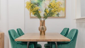 Une table à manger ornée d’un vase de fleurs jaunes, entourée de chaises recouvertes d’un tissu vert.