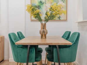 Ein Esstisch mit einer Vase gelber Blumen, umgeben von grünen, gepolsterten Stühlen.