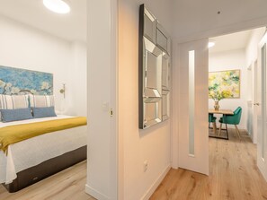 Quarto de hotel moderno com cama, um espelho grande, um quadro e um espaço de refeições com mesa e cadeiras.