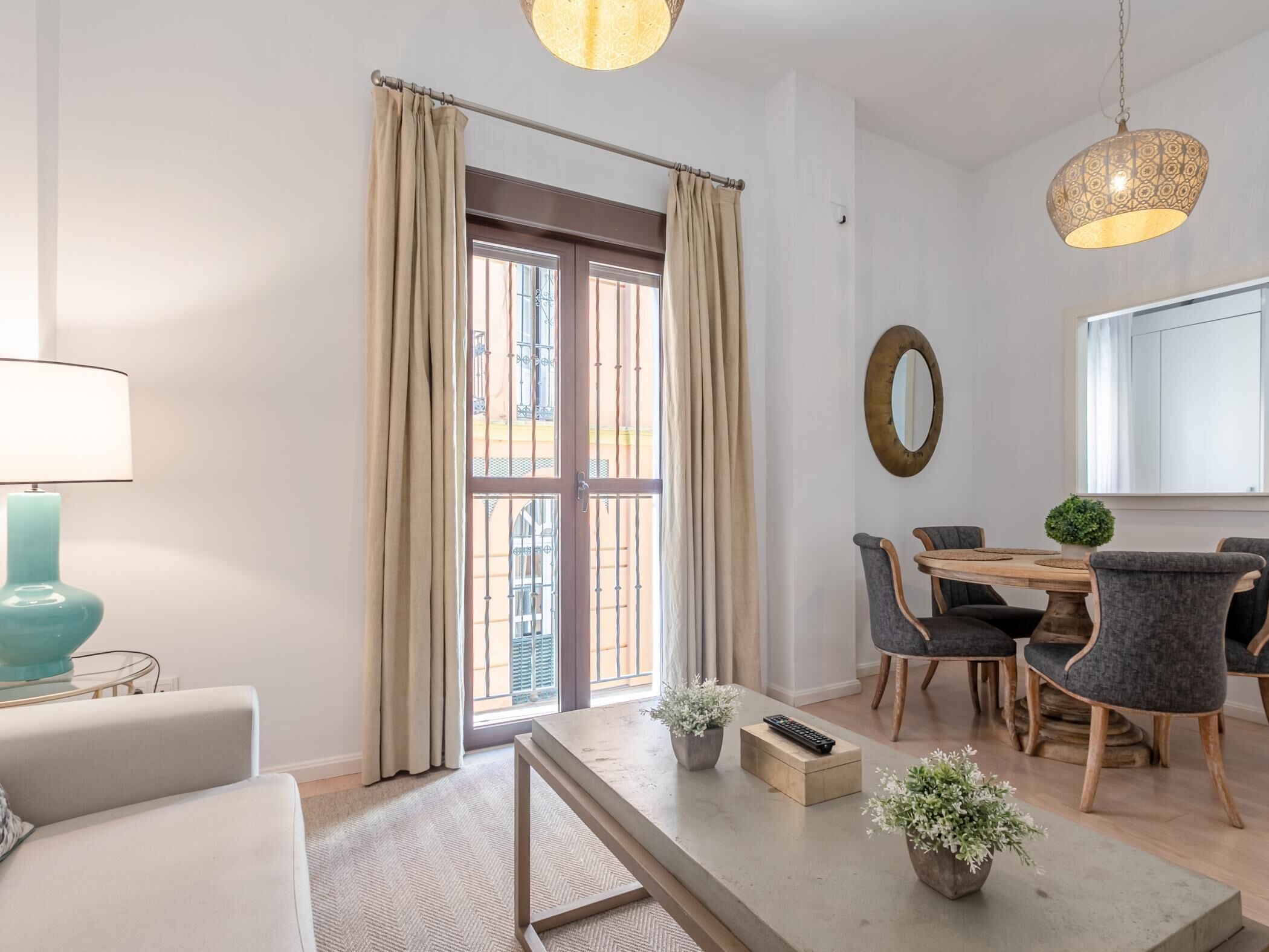 Un salon moderne comprenant un canapé, une table basse, une table à manger avec des chaises, une lampe et une grande fenêtre avec des rideaux.