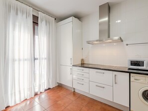 A modern kitchen with white cabinets, a stainless steel range hood, a microwave, and a washing machine. - Hommyhome San Esteban 101 (Sevilla)