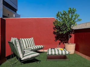 A rooftop terrace with a green lawn, a striped lounge chair, a small table with a cushion, and a potted plant. - Hommyhome San Esteban 101 (Sevilla)