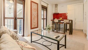 Uma sala de estar moderna com uma mesa de centro de vidro, um sofá e uma área de cozinha com painel vermelho.