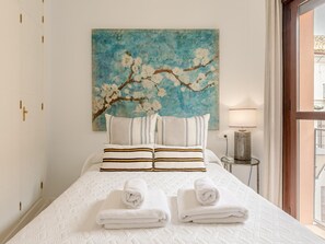 Ein Hotelzimmer mit einem Bett, Kissen, einem Gemälde, einem Nachttisch und einer Lampe.