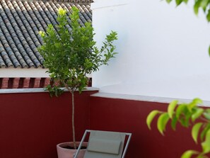 A potted tree on a balcony with a tiled roof and a red wall. - Hommyhome San Esteban 102 (Sevilla)