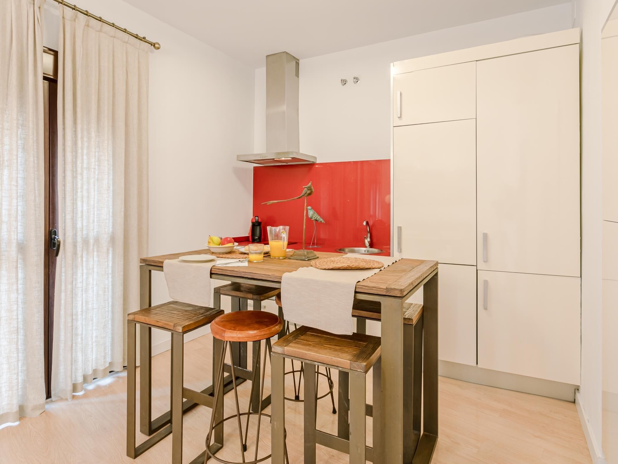 A compact kitchen with a dining table, chairs, and a red accent wall.