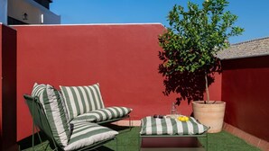 Um terraço no telhado com gramado verde, uma cadeira de lounge listrada, uma mesinha com almofada e um vaso de planta.