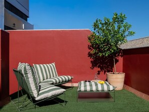 Eine Dachterrasse mit einem grünen Rasen, einem gestreiften Liegestuhl, einem kleinen Tisch mit Kissen und einem Blumentopf.