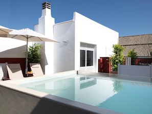 A modern outdoor pool area with a clear blue pool, white walls, and a red door. - Hommyhome San Esteban 102 (Sevilla)