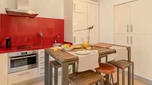 Uma cozinha compacta com painel vermelho, forno embutido e mesa de jantar de madeira com bancos.