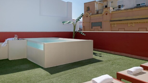 Um terraço no telhado com banheira de hidromassagem, grama sintética e vista para edifícios próximos.