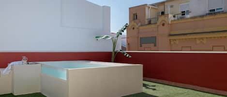 A rooftop terrace with a hot tub, lounge chairs, and a potted plant.