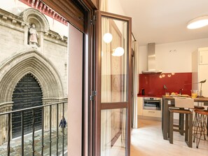 A modern kitchen with a red accent wall, a dining area with stools, and a view of a historic building with a large arched door. - Hommyhome San Esteban 102 (Sevilla)