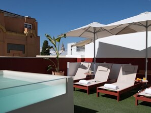 Una terrazza sul tetto con piscina, poltrone relax e ombrelloni.