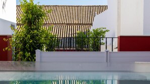 Une piscine dont l’eau est si claire qu’elle reflète parfaitement l’environnement, un toit recouvert de tuiles et un mur blanc.