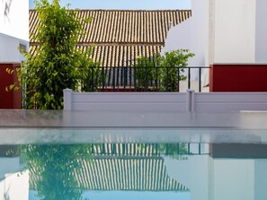 Ein Schwimmbecken mit spiegelnder Oberfläche, einem Ziegeldach und einer weißen Wand.