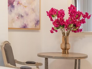 Ein runder Holztisch mit einer Vase voller rosa Blumen, einem Stuhl und einem Bild an der Wand.